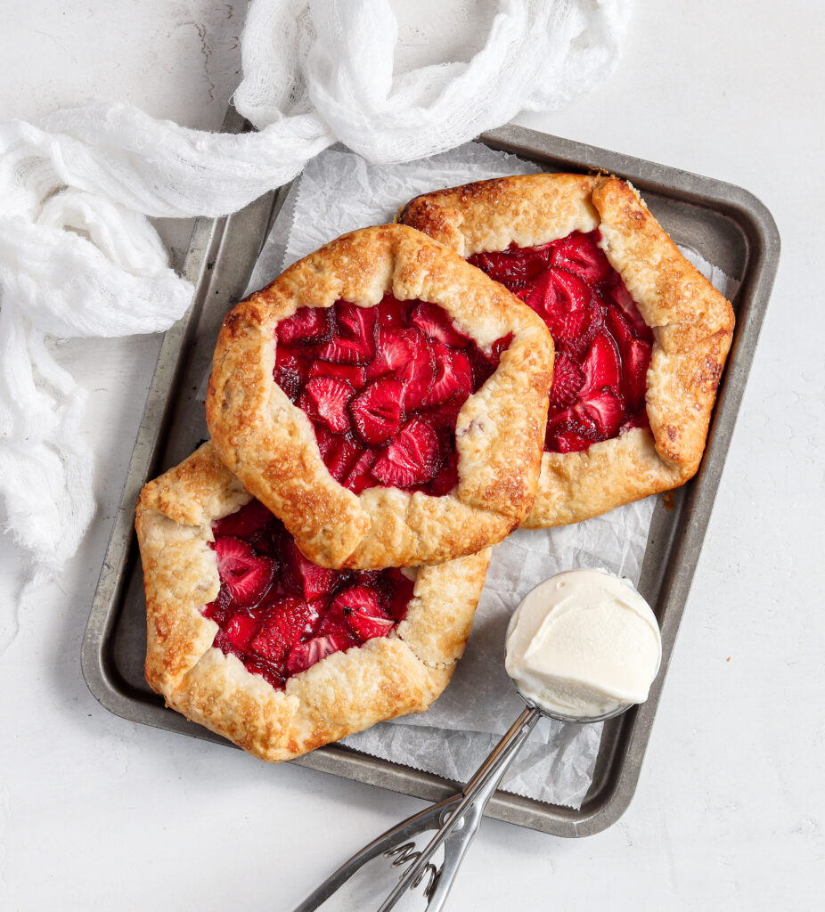 Mini Strawberry galette's on a baking tray with a scoop of ice cream