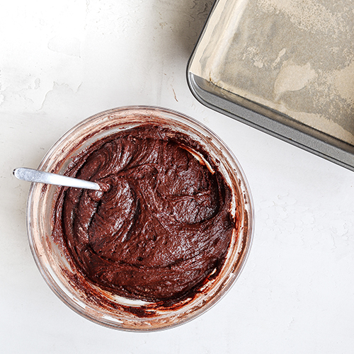 A bowl of brownie batter and a lined baking pan