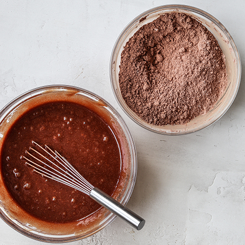 Two bowls, one with melted chocolate, butter, eggs, the other with flour and cocoa