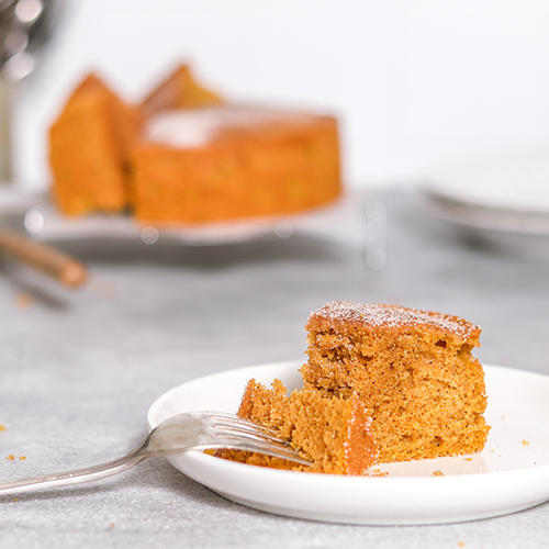 Slice of pumpkin spice tea cake on a plate with full cake in the background