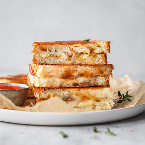 Caramelized onion grilled cheese sandwiches stacked on a plate