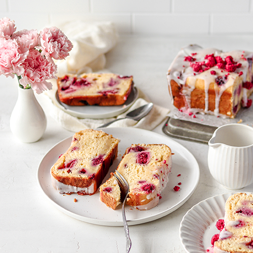 Raspberry loaf cake sliced and sitting on three plates with a vase of flowers