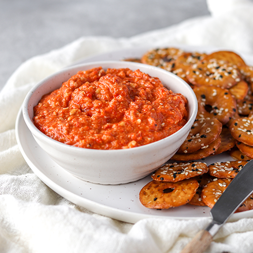 Pepper pesto dip in a bowl on a plate with crackers