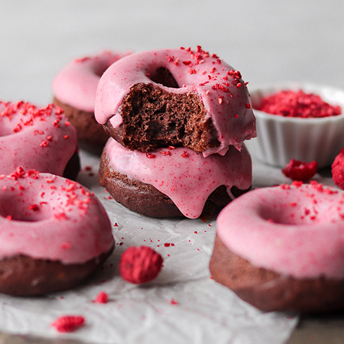 Chocolate raspberry donut stacked on a baking tray lined with parchment paper