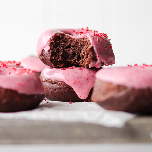 Baked chocolate donuts stacked on each other, the top donut has a bite taken out of it